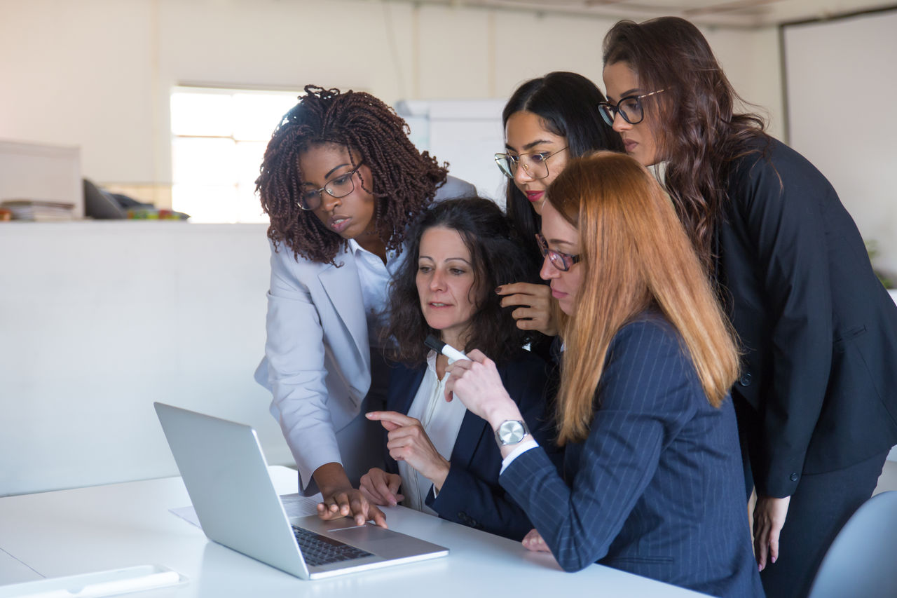 Businesswomen discussing project at laptop computer. Group of concentrated multiethnic female colleagues using laptop computer in office. Business and technology concept, Businesswomen discussing project at laptop computer. Group of concentrated multiethnic female colleagues using laptop computer in office. Business and technology concept